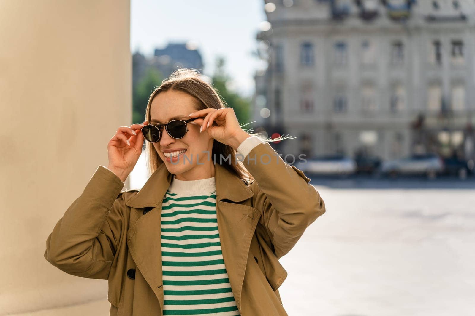 Smiling woman puts on sunglasses outside in the city.