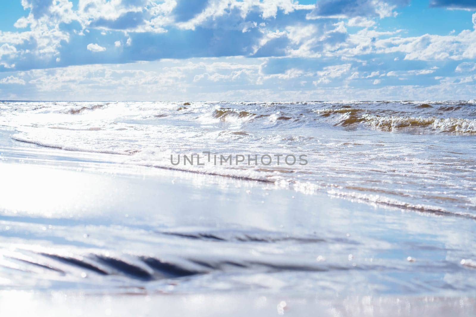 Blue sky with white clouds almost merges with sea waves with foam rolling on shore. Meditation and relaxation. Interior paintings. Wonderful moments of life. Tourism and travel. Rest and pleasure.
