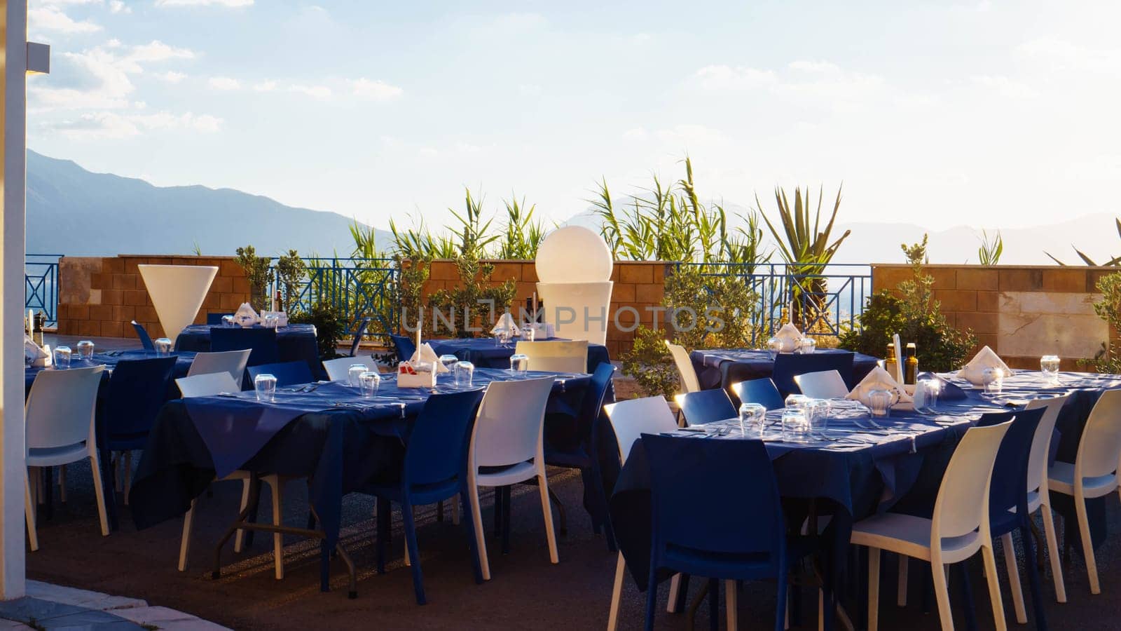 Restaurant, cafe on outdoor terrace with view of sky and mountains. Tables set with blue linen and white dishes. Italian style. Tourism and travel. Enjoying life. Beautiful places.