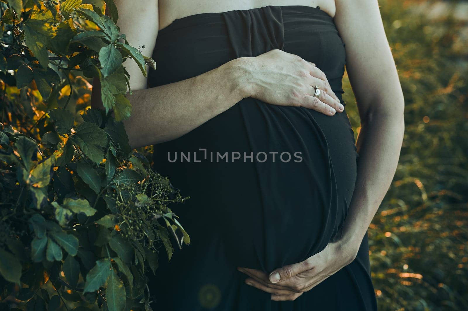Pregnant woman hugging her tummy standing outdoors surrounded by nature. Pregnancy, expectation, motherhood concept