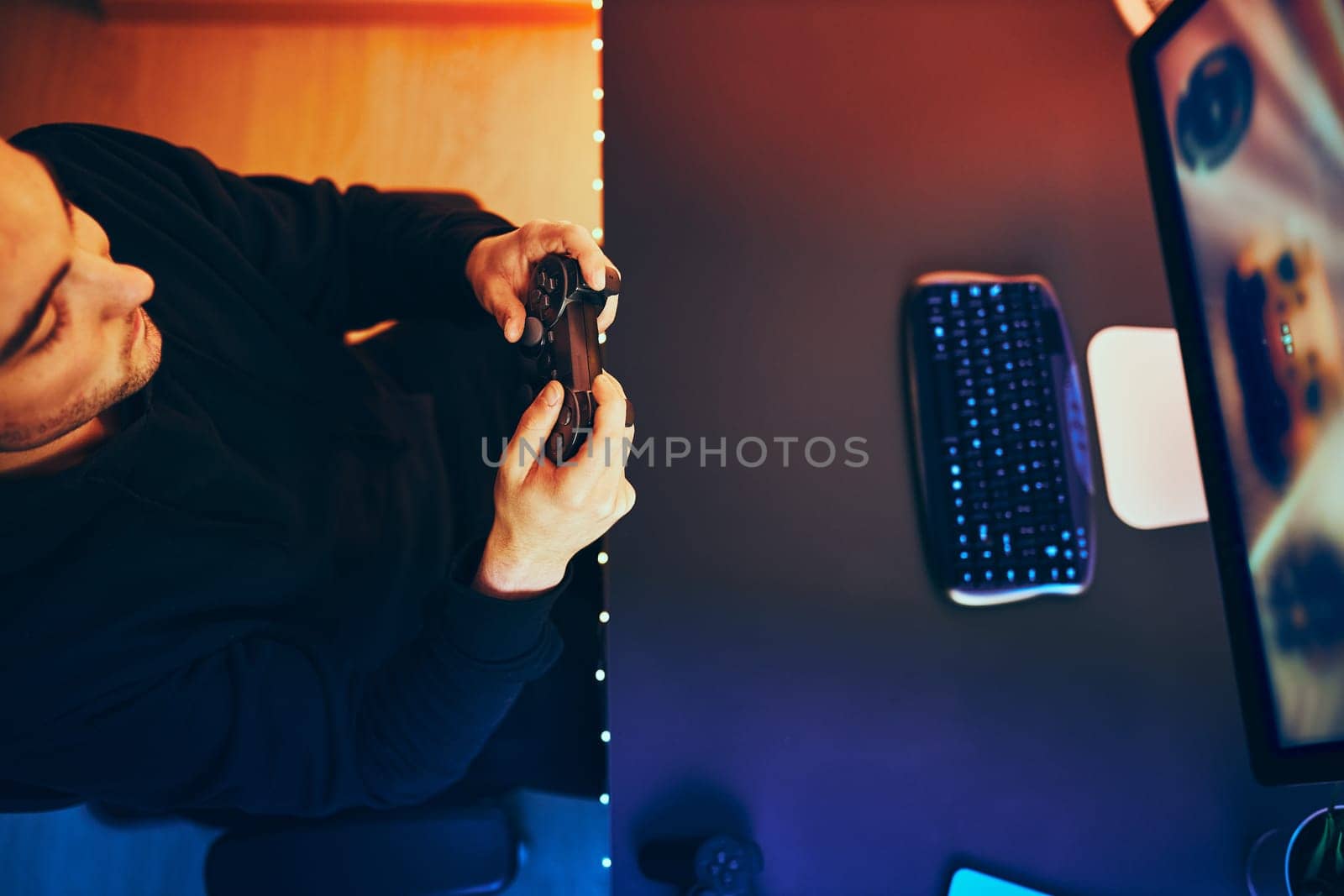 Man playing video game at home. Gamer holding gamepads sitting at front of screen. Streamer playing online in dark room lit by neon lights. Competition and having fun