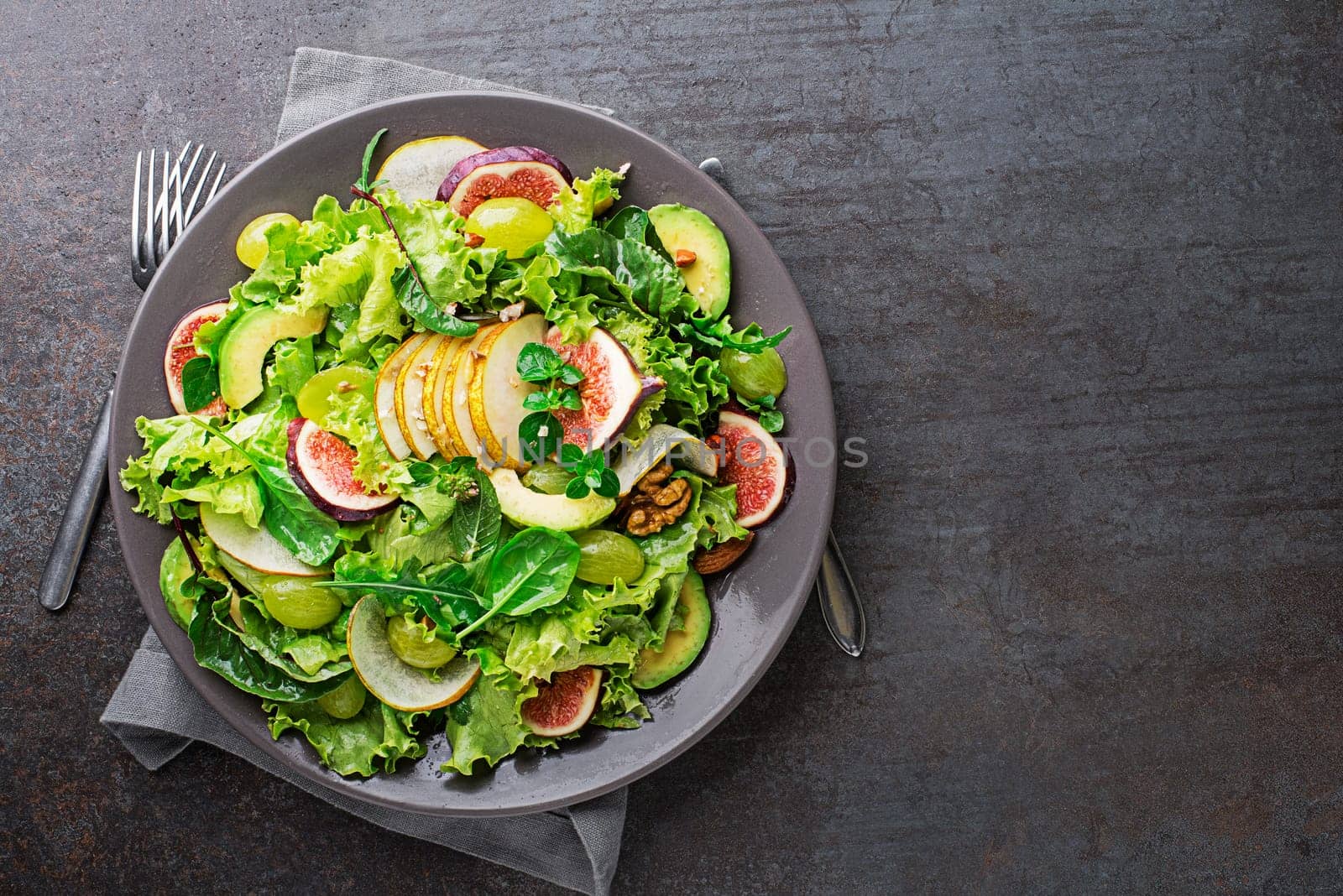 Fresh green leafy salad with fruits and nuts on grey table background. Concept for a tasty and healthy meal