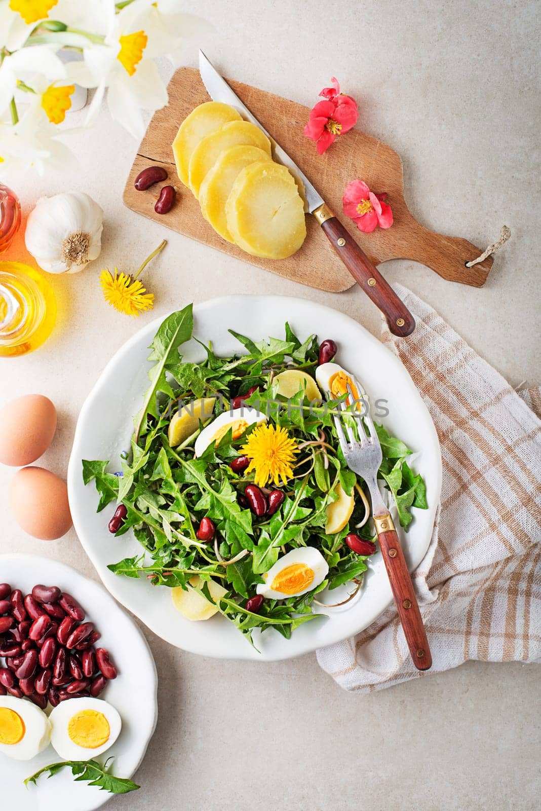 Dandelion salad with eggs, potato and beans on bright table background closeup
