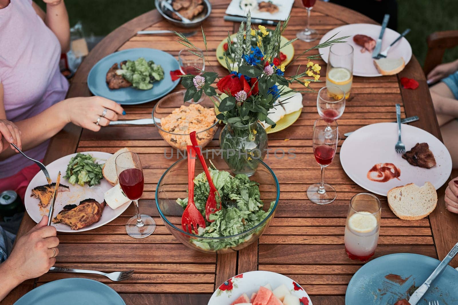Family having a meal from grill during summer picnic outdoor dinner in a home garden. Close up of people sitting at a table with food and dishes