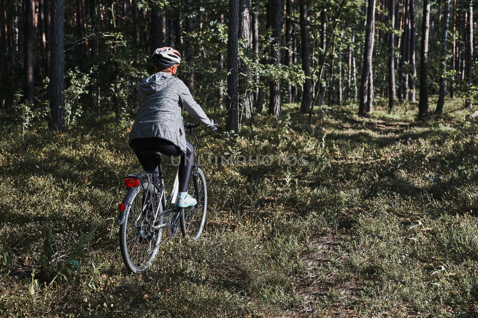 Active woman cycling on forest road. Female riding bicycle off-road route on summer vacation day. Woman wearing bicycle helmet and gloves