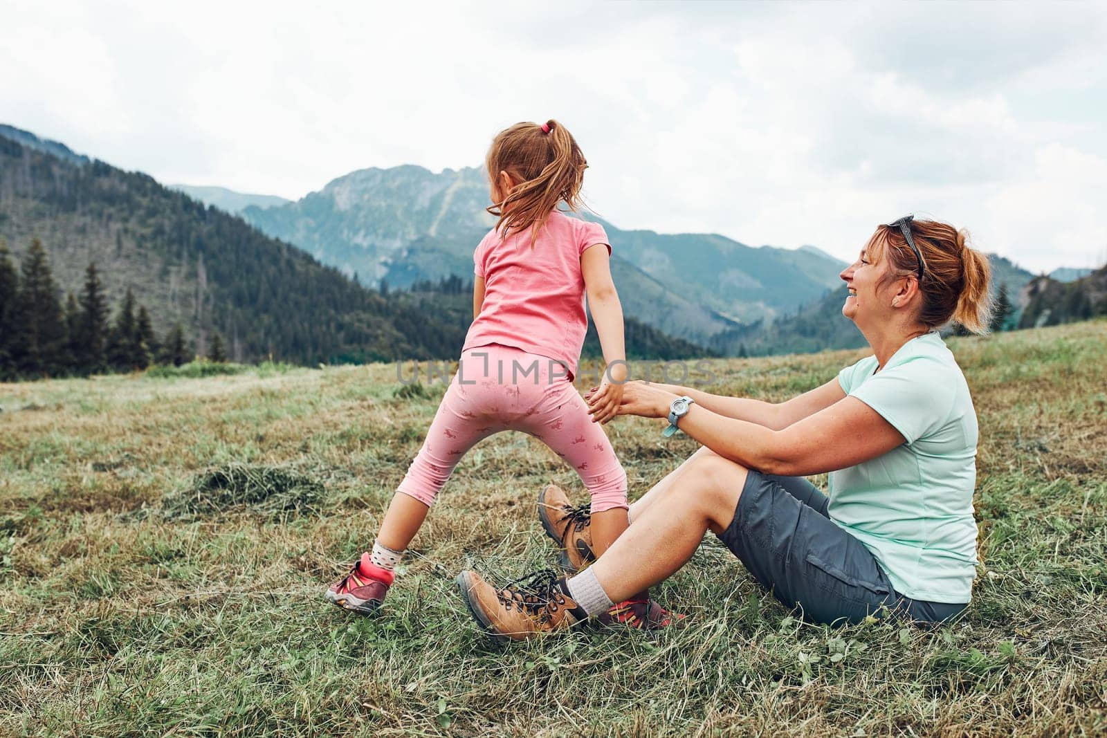 Little girl laying playing on grass enjoying summer day. Happy child playing in the field during vacation trip in mountains