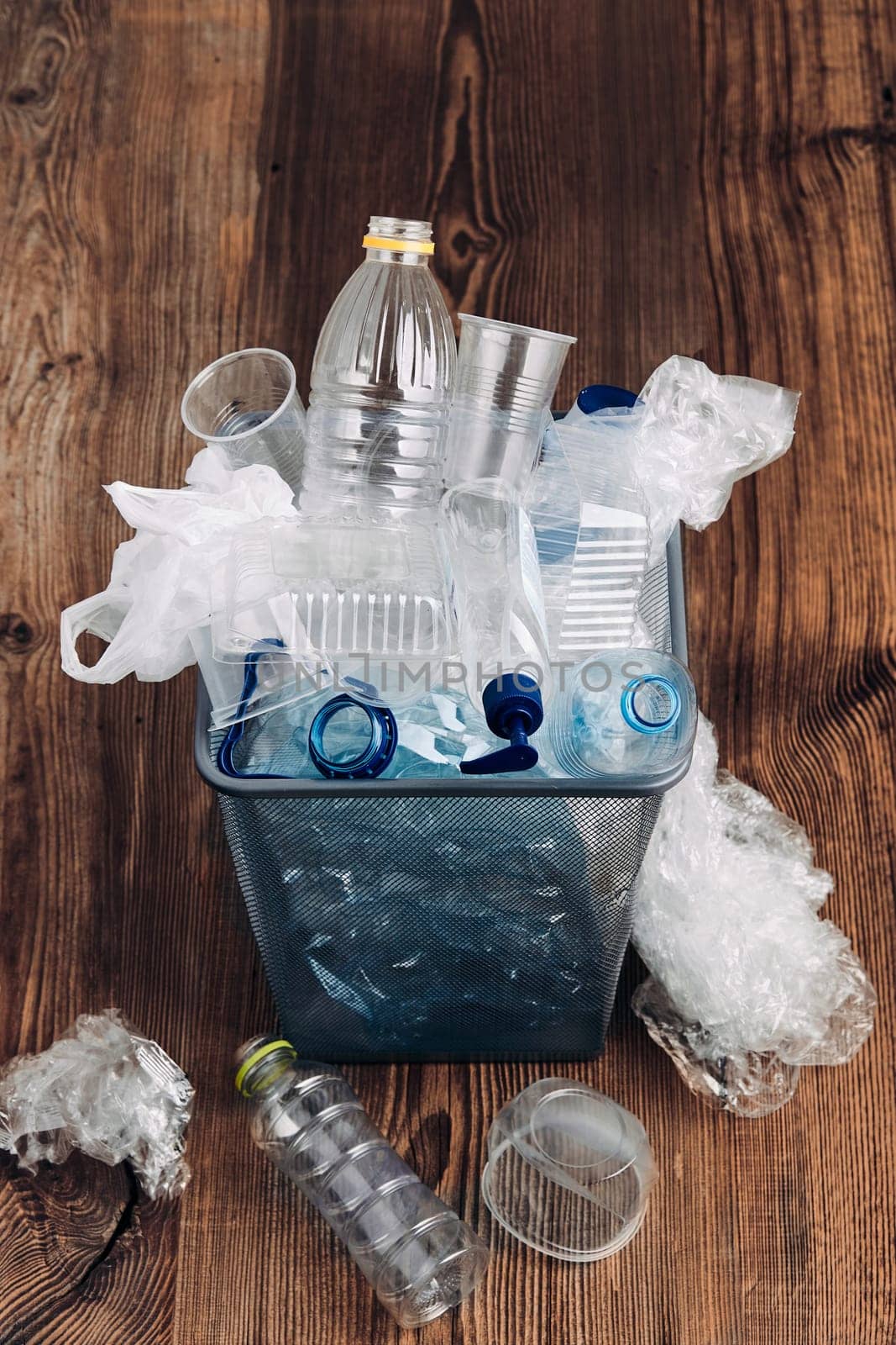Heap of plastic bottles, cups, bags collected to recycling and scattered around a metal bin. Concept of plastic pollution and too many plastic waste. Trash with used plastic packagings over grey background with copy space at the top
