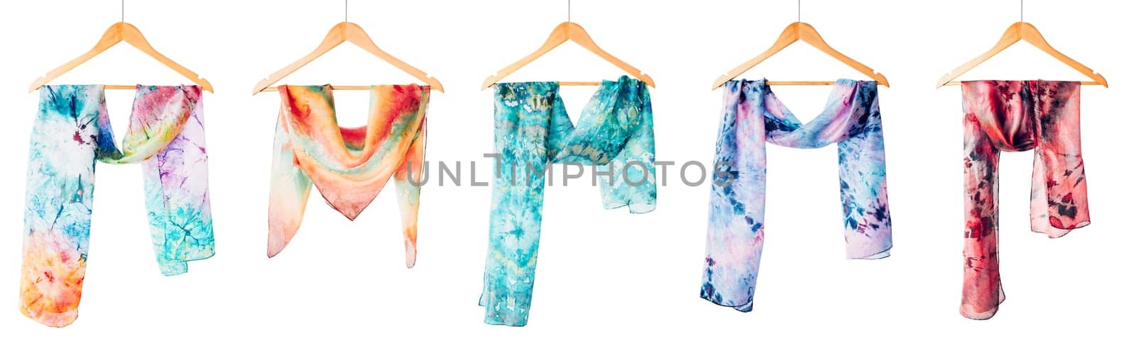 Silk colourful hand painted tied scarves hung on hangers over white background. Woman fashion, tying a scarf, wearing a scarves. Stylish ways to tie and wear scarves