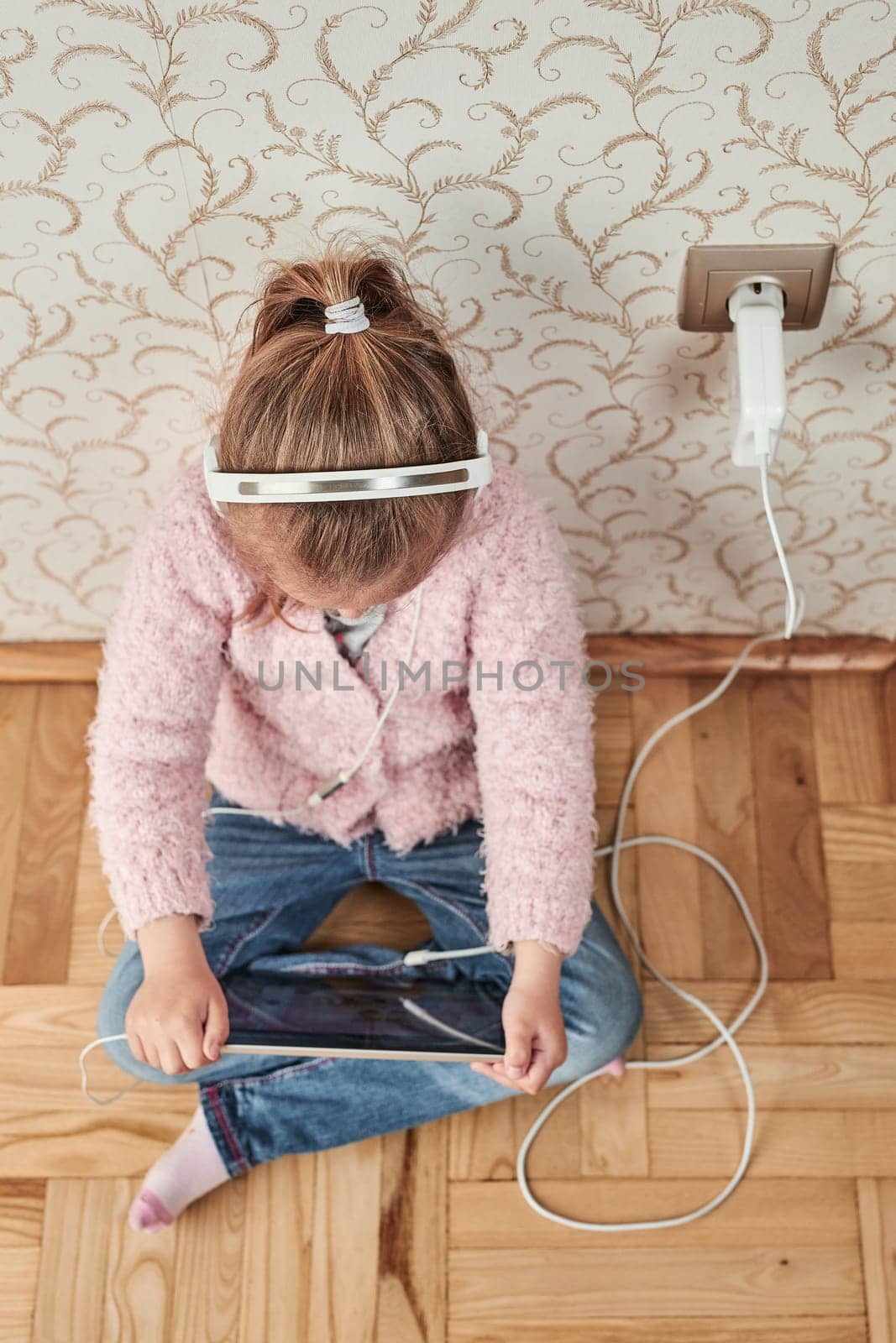 Little girl preschooler learning online solving puzzles playing educational games listetning to music and sounds using tablet and headpphones at home during pandemic quarantine