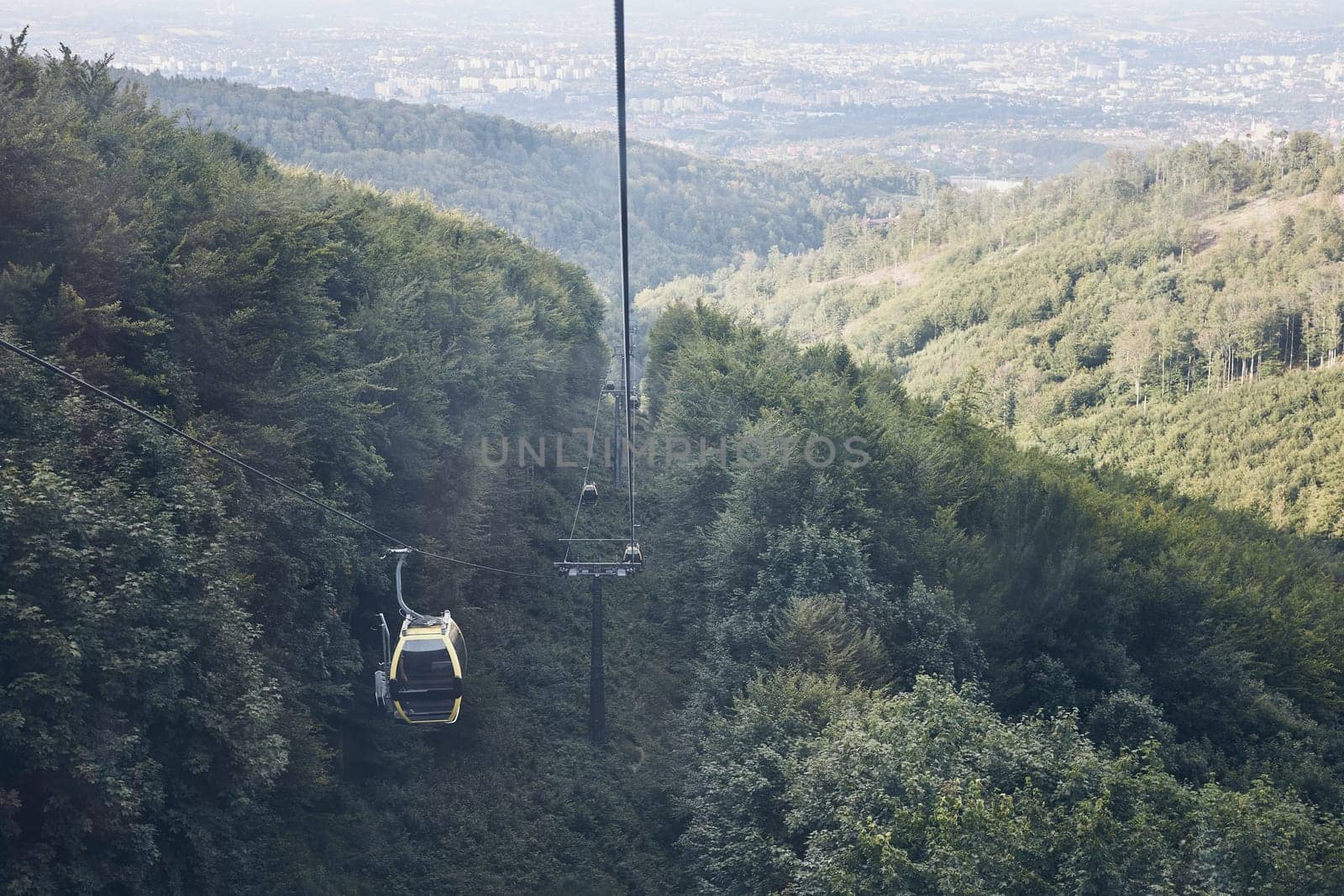 Cable car go to top of mountain among trees in forest on summer sunny day. Panoramic view of valley at mountain