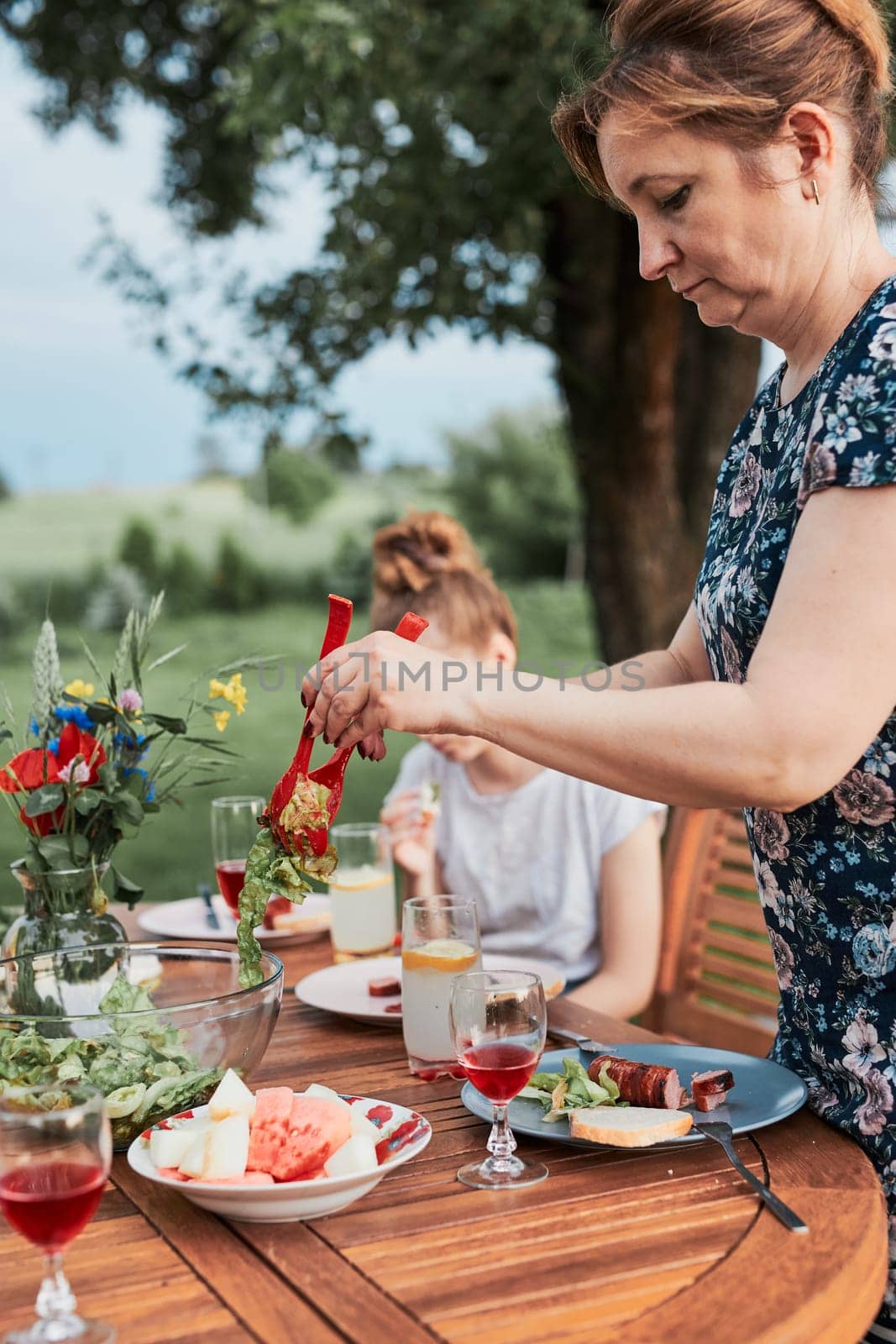 Woman having a meal from grill during summer family picnic outdoor dinner in a home garden. Close up of people sitting at a table with food and dishes