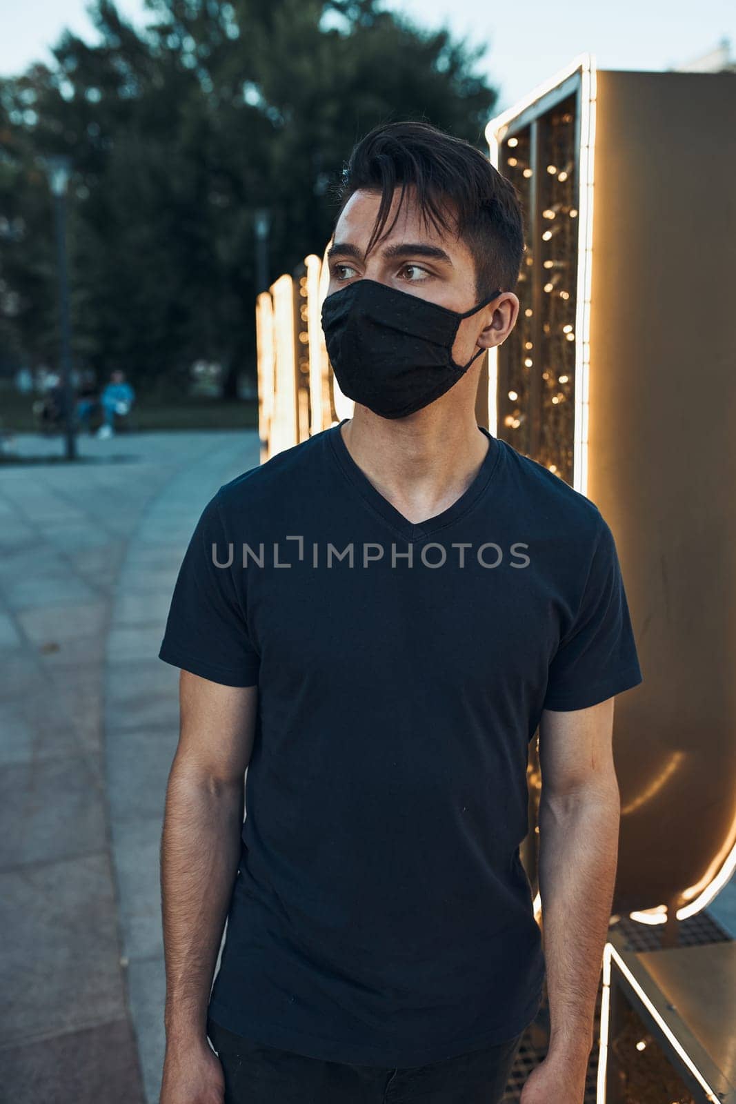 Young man standing in the city center in the evening looking away wearing the face mask to avoid virus infection and to prevent the spread of disease in time of coronavirus