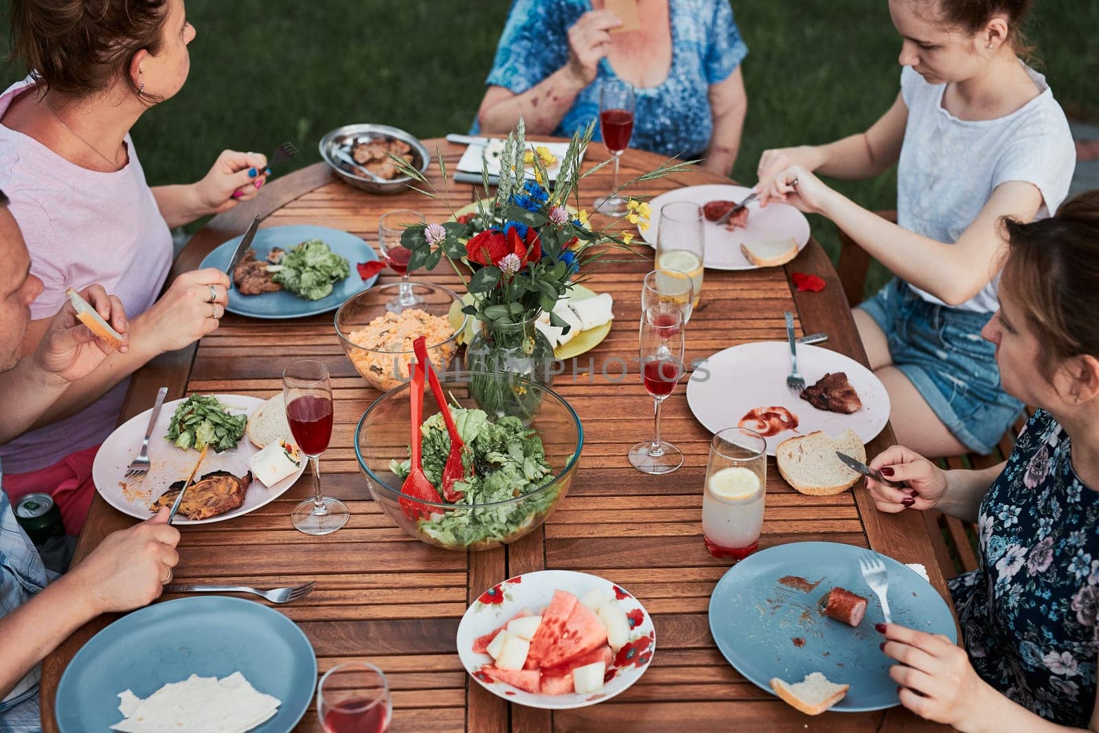 Family having a meal from grill during summer picnic outdoor dinner in a home garden. Close up of people sitting at a table with food and dishes