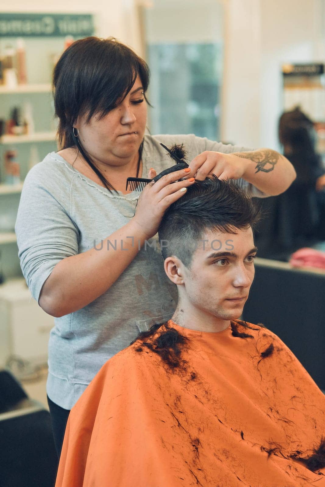 Hairdresser haircutting styling young man's hair in barbershop. Young woman working as a hairdresser in hair salon. Real people, authentic situations