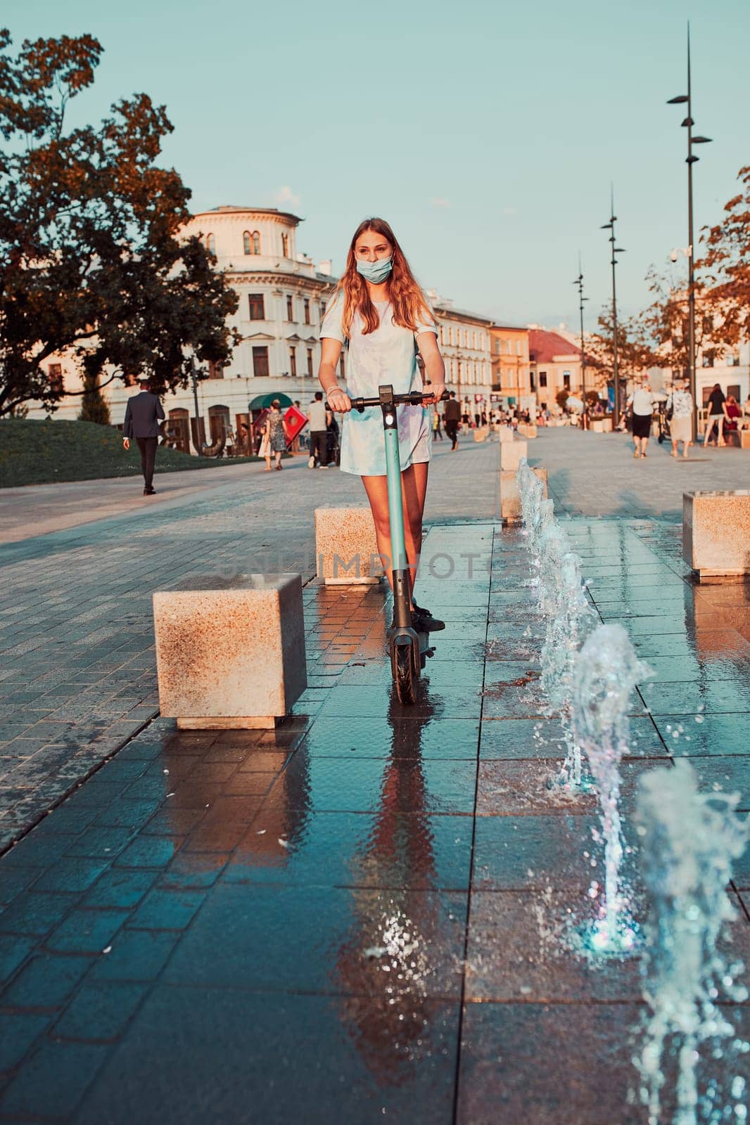 Young woman riding an electric scooter in the city center. Woman wearing the face mask to avoid virus infection and to prevent the spread of disease in time of coronavirus. Candid people, real moments, authentic situations