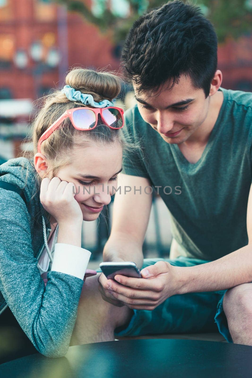 Couple of friends, teenage girl and boy,  having fun with smartphones, sitting in center of town, spending time together