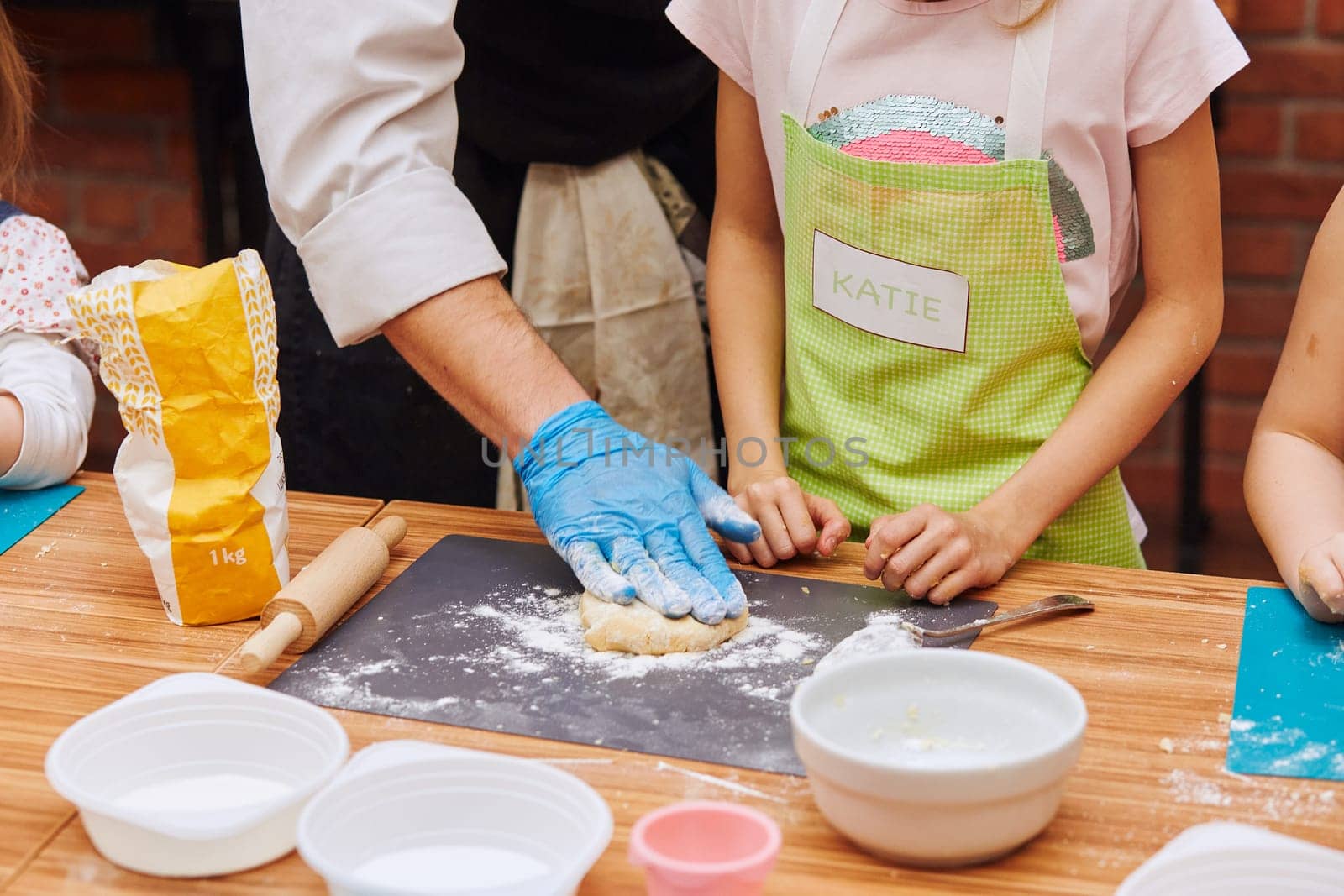 Girl with chefs help kneading the dough for baking the cake. Kid taking part in baking workshop. Baking classes for children,  aspiring little chefs. Learning to cook. Combining and stirring prepared ingredients. Real people, authentic situations
