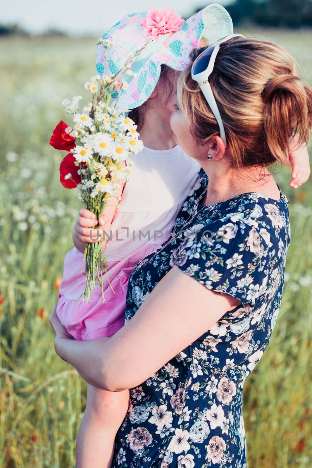 Mother and her little daughter in the field of wild flowers. Little girl picking the spring flowers for her mom for Mother's Day in the meadow. Girl handing the flowers to her mom. Nature scene, family time