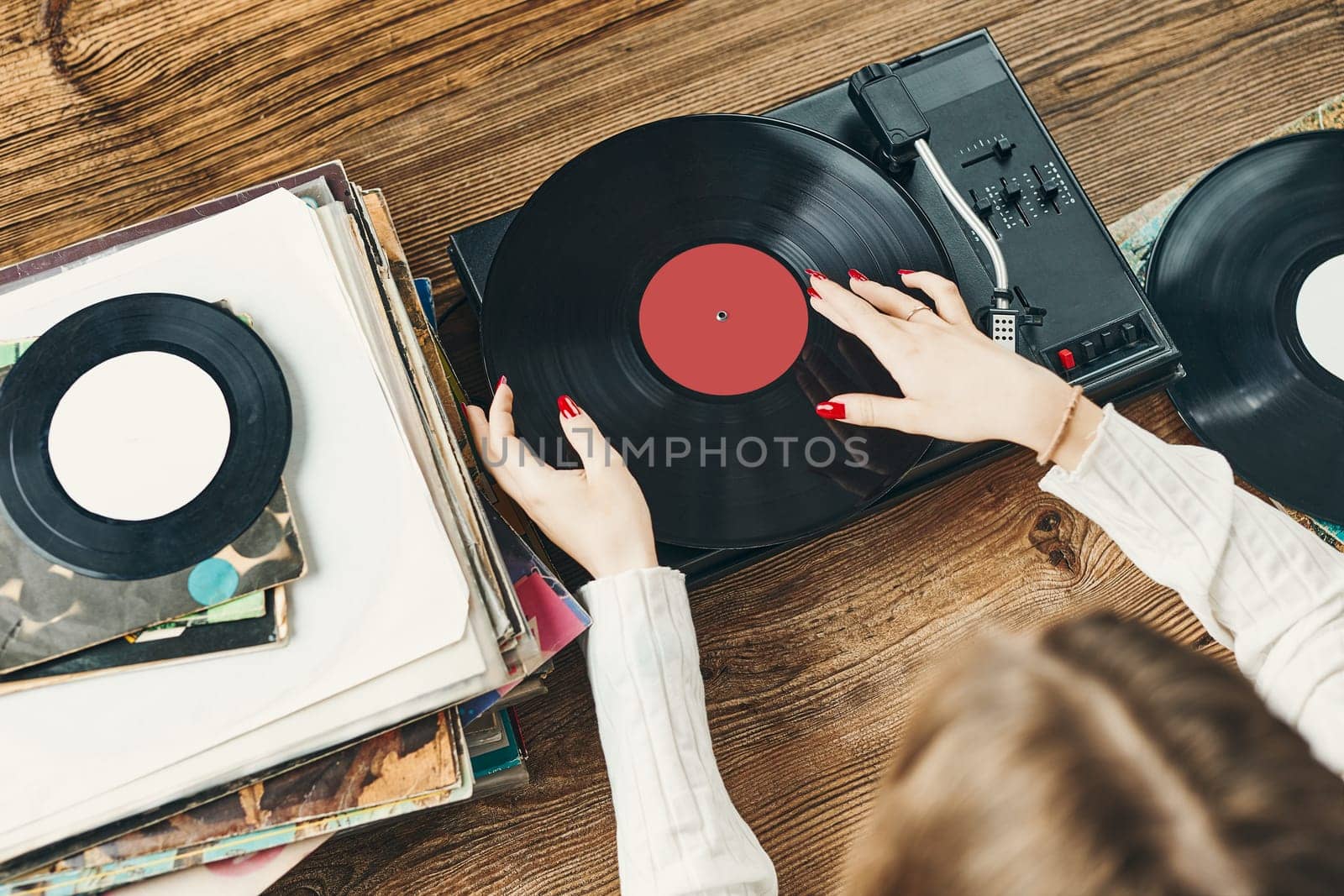 Young woman listening to music from vinyl record player. Playing music on turntable player. Female enjoying music from old record collection at home. Stack of analog vinyl records. Retro and vintage music style. Music Passion and hobby