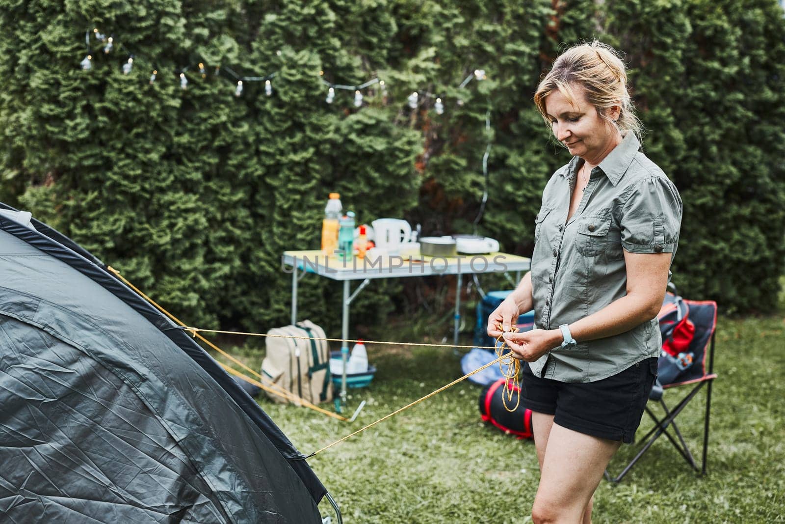 Woman putting up a tent at camping during summer vacation. Female preparing campsite to rest and relax. Spending vacations outdoors close to nature