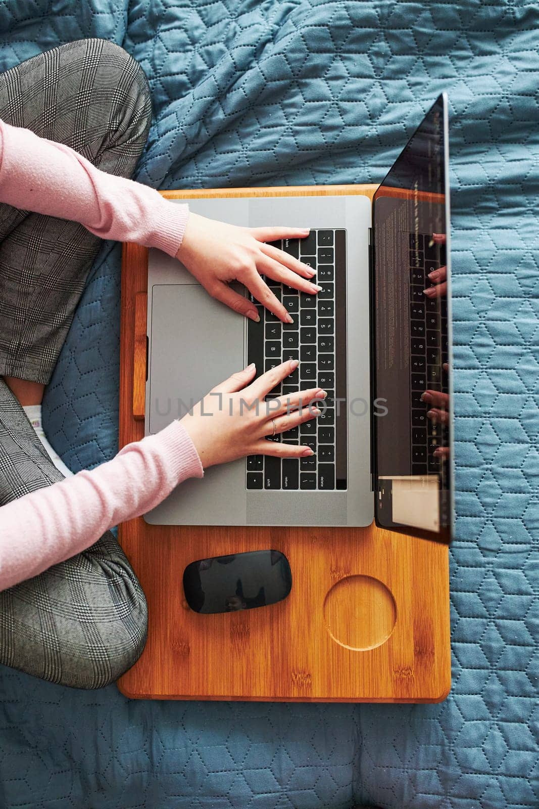 Teenage girl working on school tasks remotely on her laptop from home during COVID-19 quarantine. Online course lessons. Learning remotely. Girl sitting on bed in front of computer. View from above