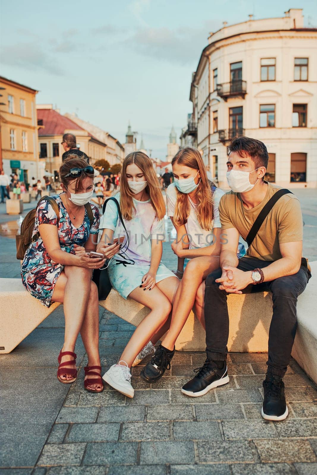 Family spending time together sitting in the city center. Girls wearing the face masks to avoid virus infection and to prevent the spread of disease in time of coronavirus