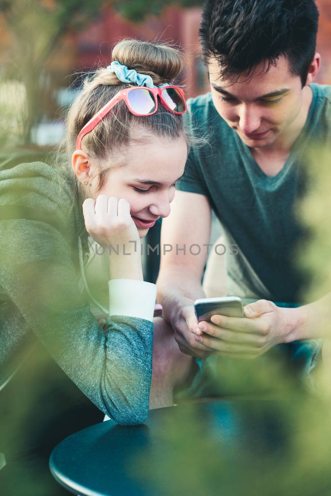 Couple of friends, teenage girl and boy,  having fun with smartphones, sitting in center of town, spending time together