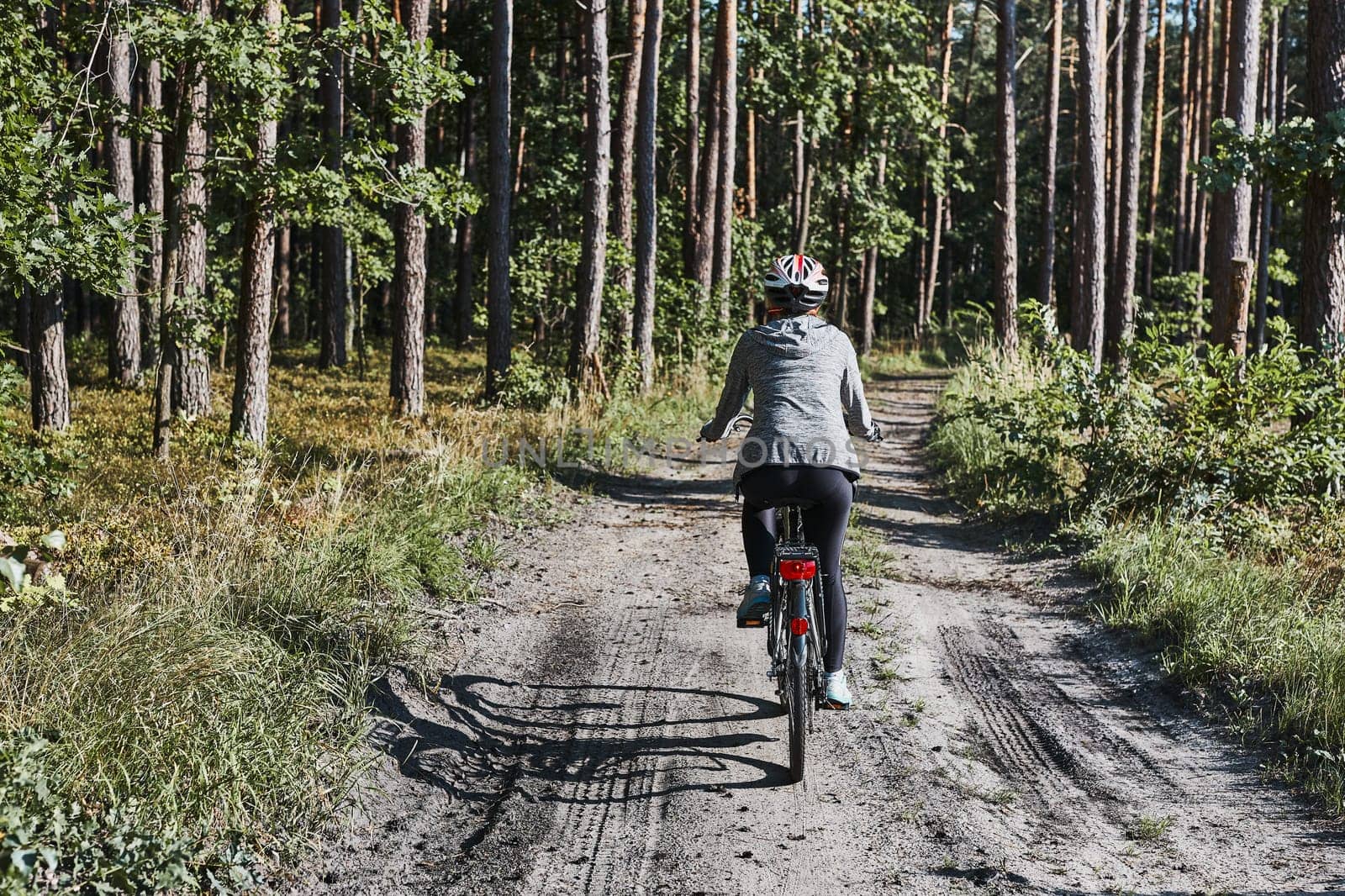 Active woman cycling on forest road. Female riding bicycle off-road route on summer vacation day. Woman wearing bicycle helmet and gloves