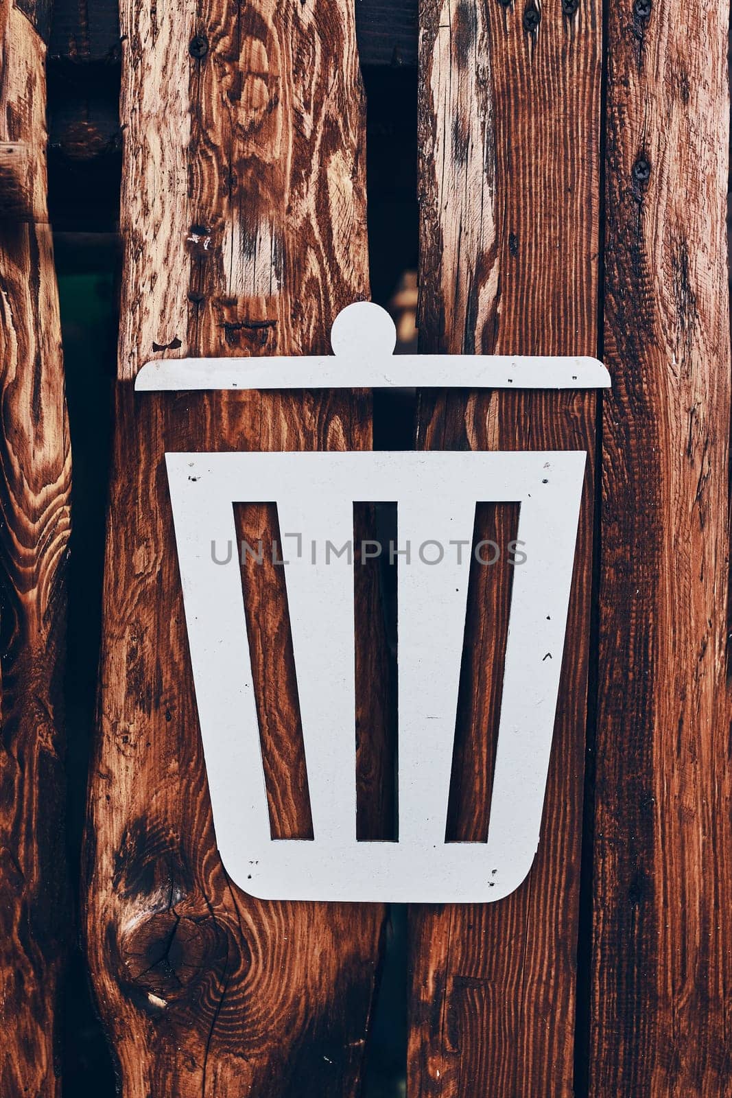 Trash bin sign on wooden plank wall. White waste basket symbol on brown background