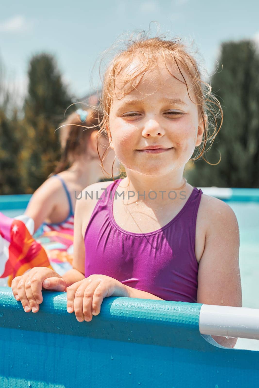 Portrait of happy smiling girl standing in a pool having fun on a summer sunny day. Close up of smiling kid looking at camera