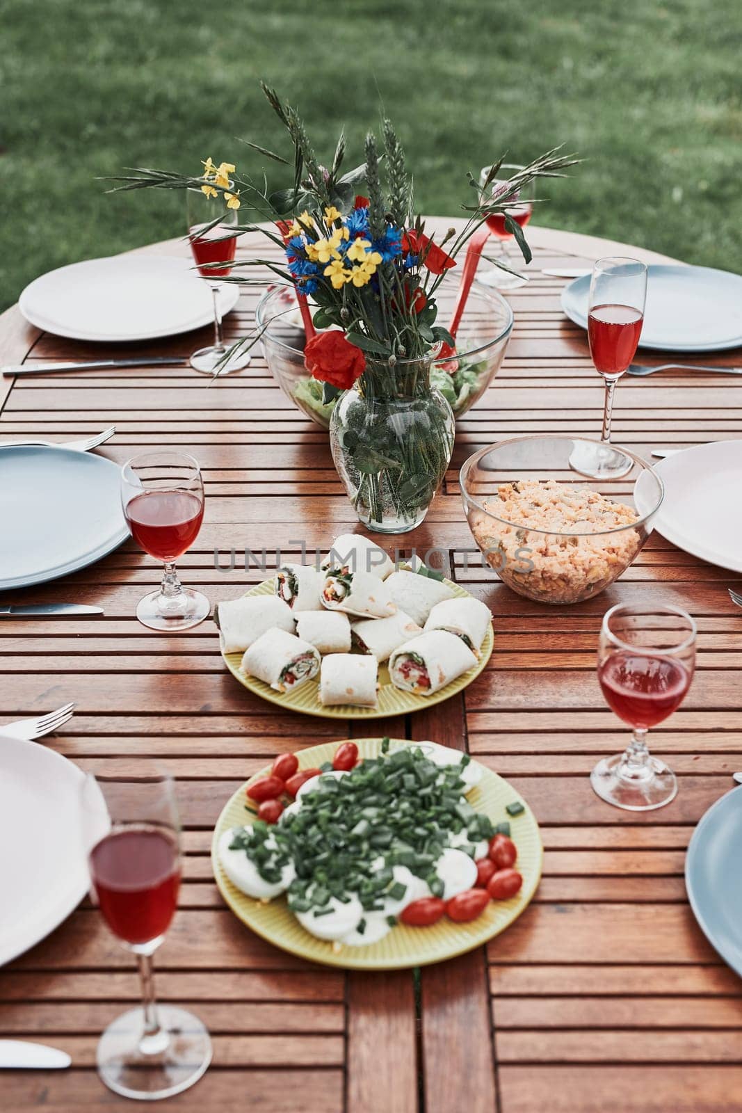 Dinner in an apple orchard garden on wooden table with salads and wine decorated with flowers. Close up of table with food prepared for family dinner