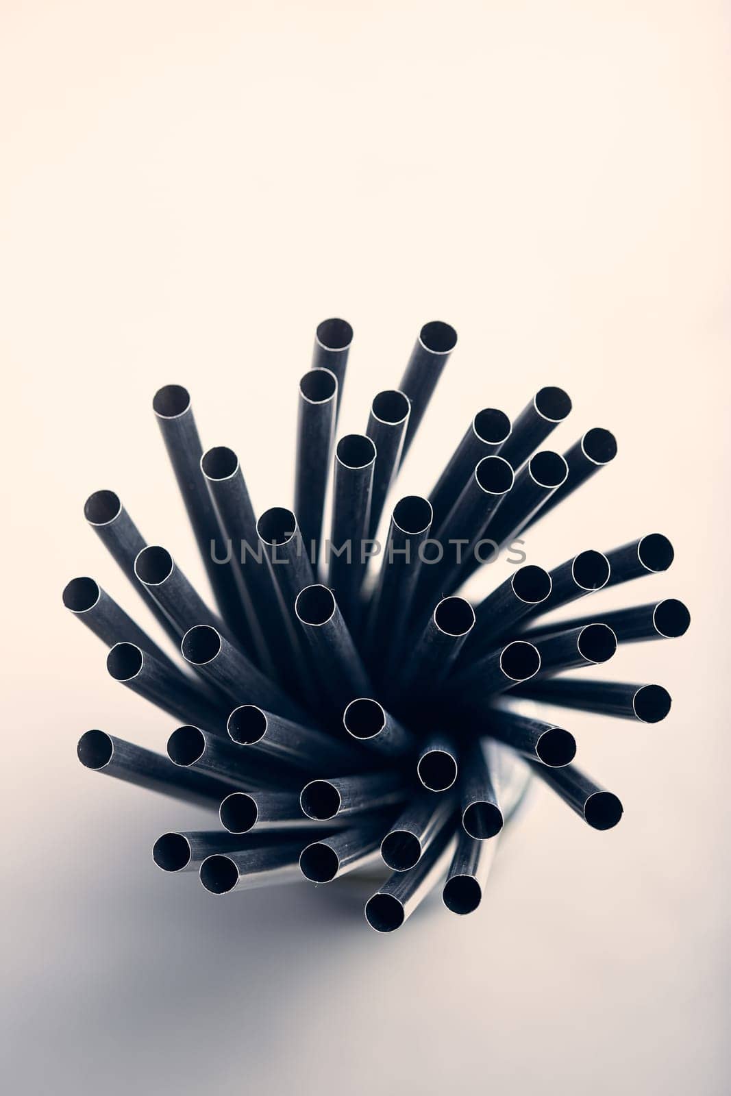 Bunch of black plastic straws scattered in container over plain grey background. Copy space for text
