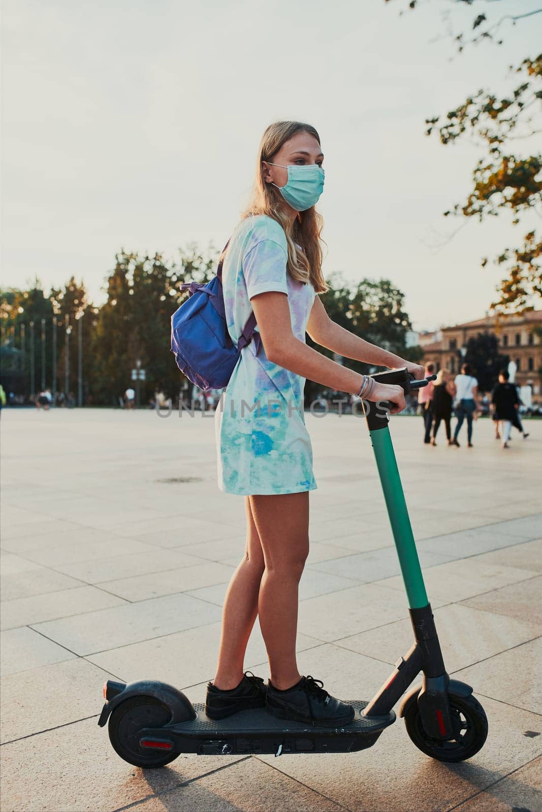 Young woman riding an electric scooter in the city center. Woman wearing the face mask to avoid virus infection and to prevent the spread of disease in time of coronavirus. Candid people, real moments, authentic situations