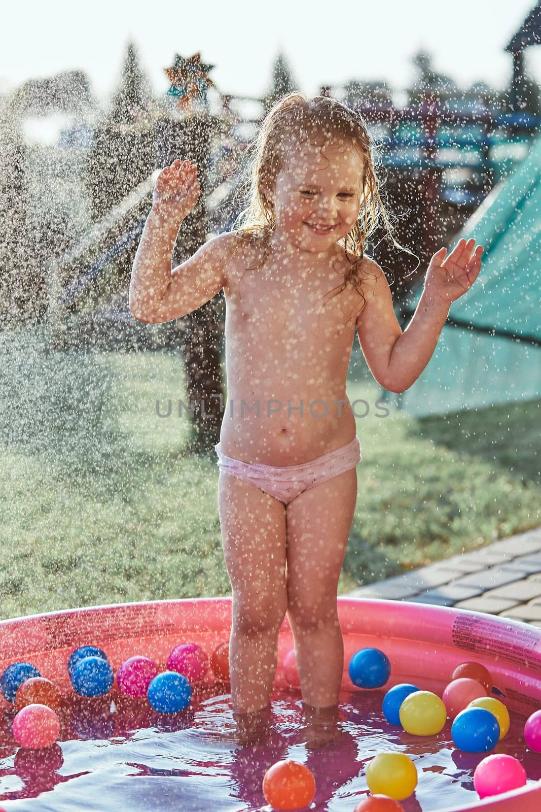 Little cute adorable girls enjoying a cool water sprayed by their father during hot summer day in backyard. Candid people, real moments, authentic situations