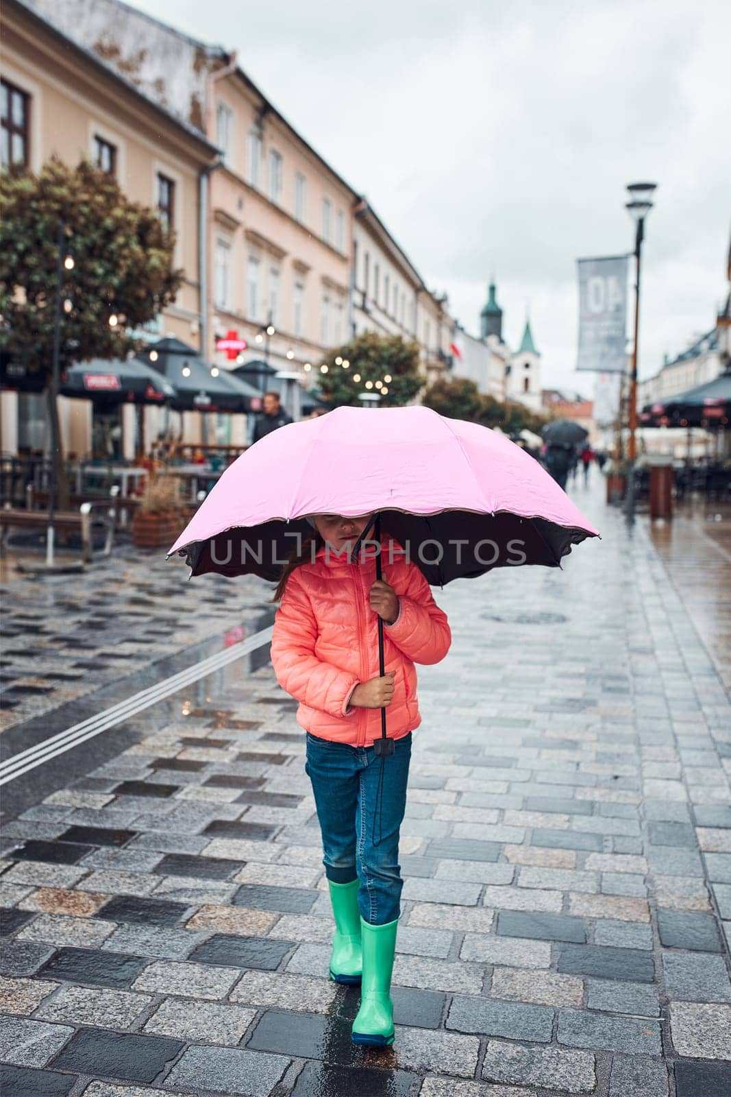 Child holding big pink umbrella walking in a downtown on rainy gloomy autumn day