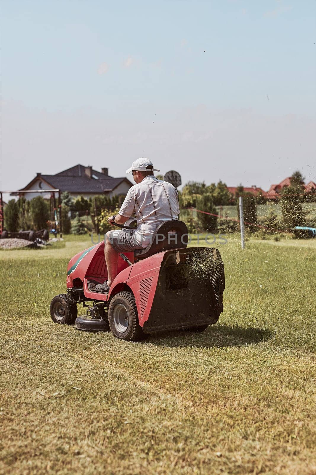 Man mowing his lawn using riding lawnmower. Man maintaining grass in his garden beside house