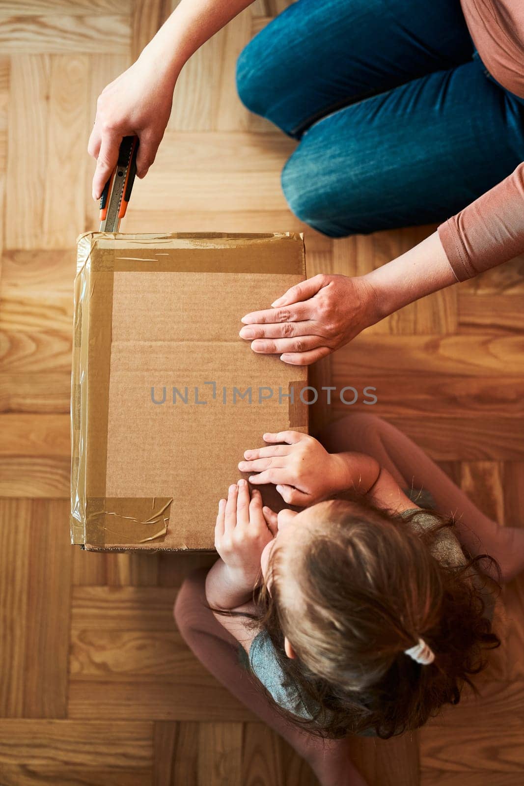 Woman unpacking a cardboard box parcel in room at home. Little girl waiting for opening a gift in package