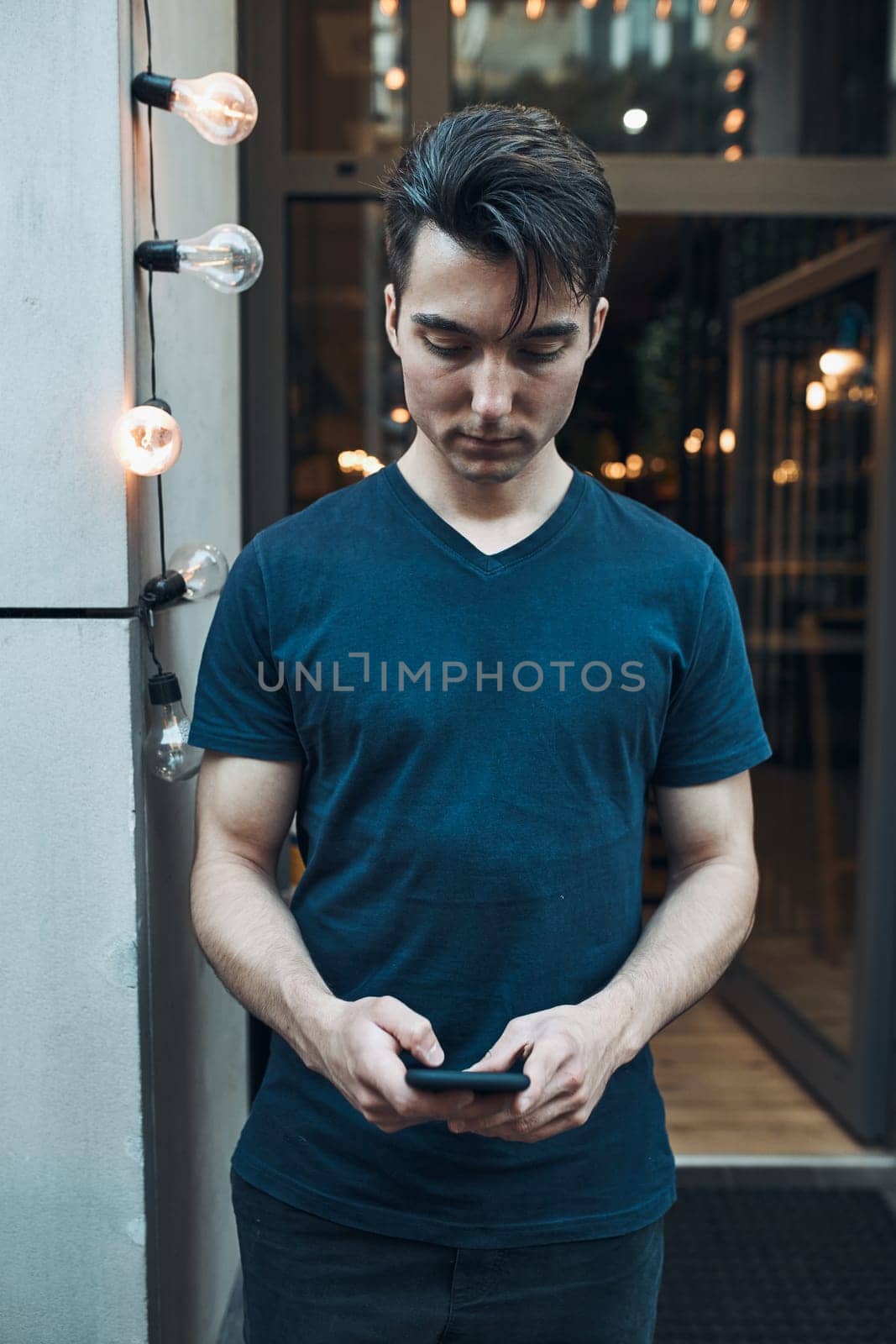 Young man standing in front of restaurant in the city center holding smartphone looking at screen