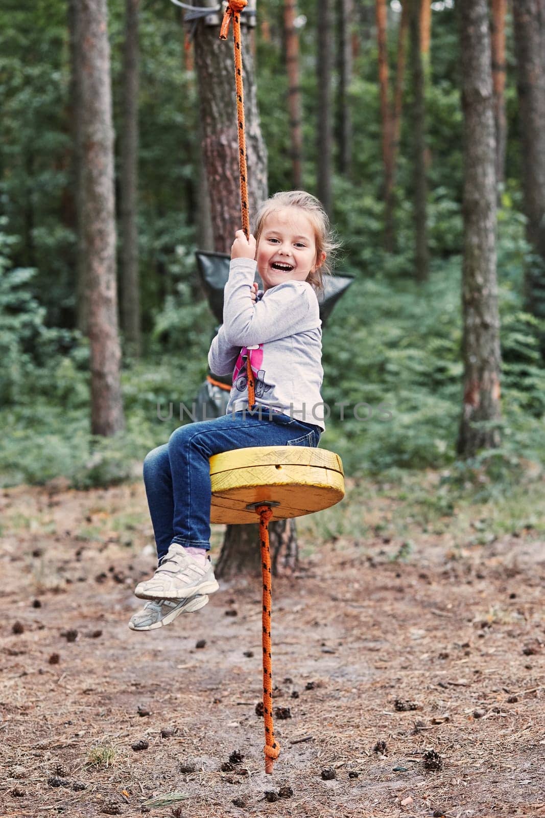 Happy girl riding on the zip line in rope park in forest while spending summer vacation. Real people, authentic situations
