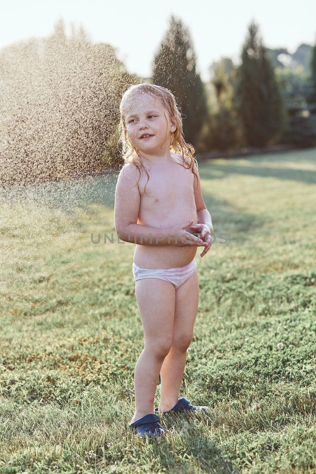 Little cute adorable girl enjoying a cool water sprayed by her mother during hot summer day in backyard. Candid people, real moments, authentic situations
