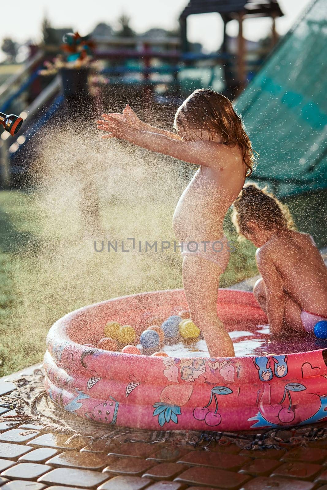 Little cute adorable girls enjoying a cool water sprayed by their father during hot summer day in backyard. Candid people, real moments, authentic situations