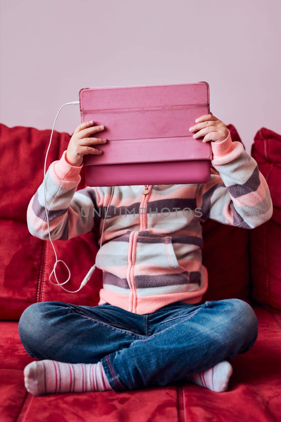 Little girl preschooler learning online solving puzzles playing educational games listetning to music and sounds using tablet and headpphones sitting on sofa at home