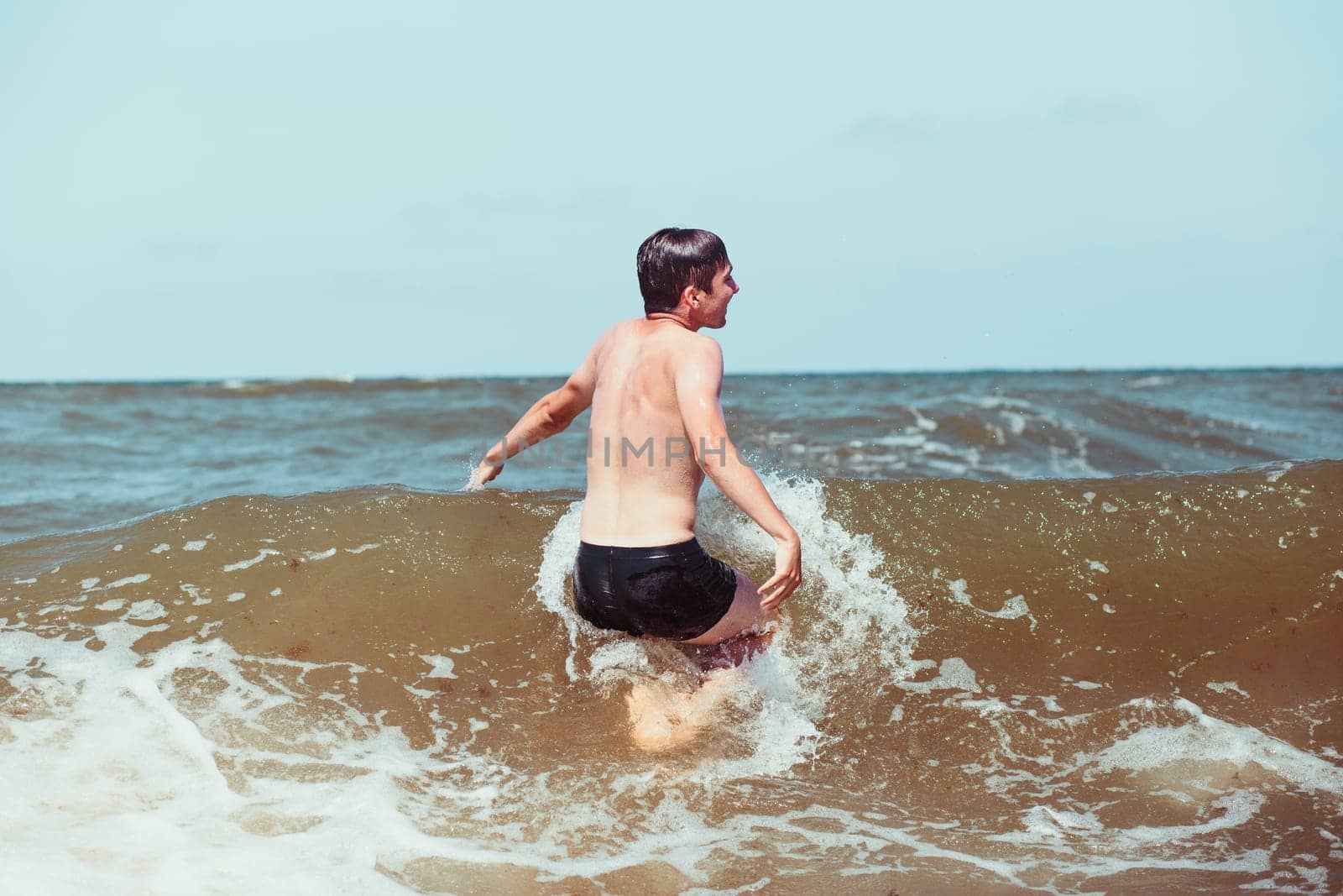 Young man enjoying the high waves in the sea during a summer vacations. Spending a summer holiday by the sea