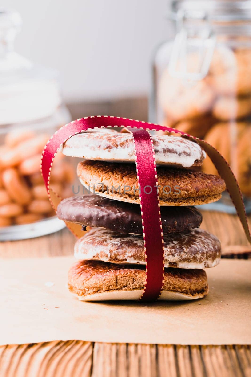 A few gingerbread cookies wrapped in red ribbon Happy Christmas on wooden table. Jars with sweets in the background. Portrait orientation