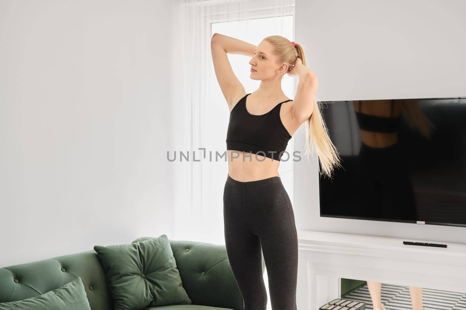 Active blonde woman does twisting exercises in bright apartment