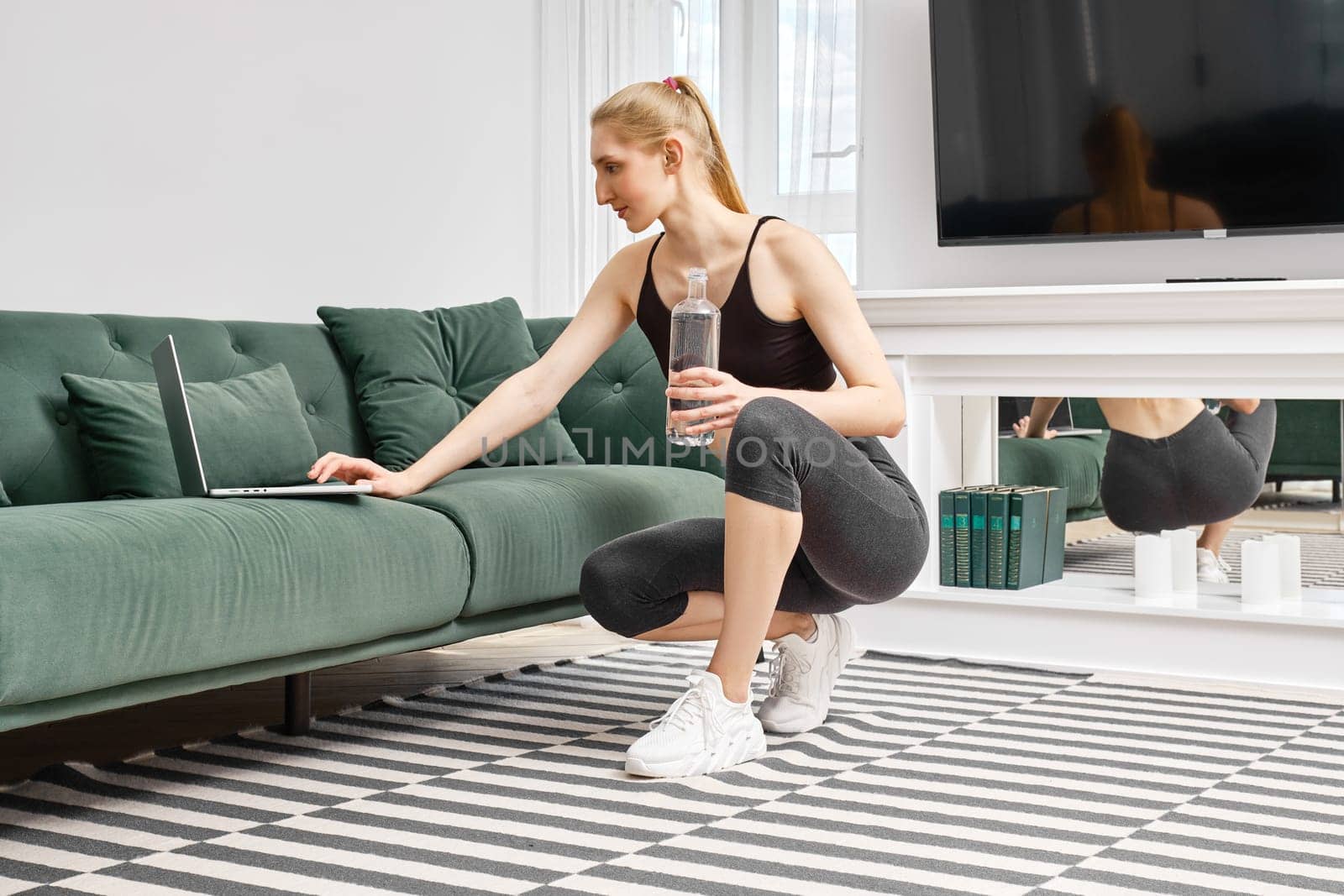 Young active woman does training exercises at home and follows an online course video on laptop