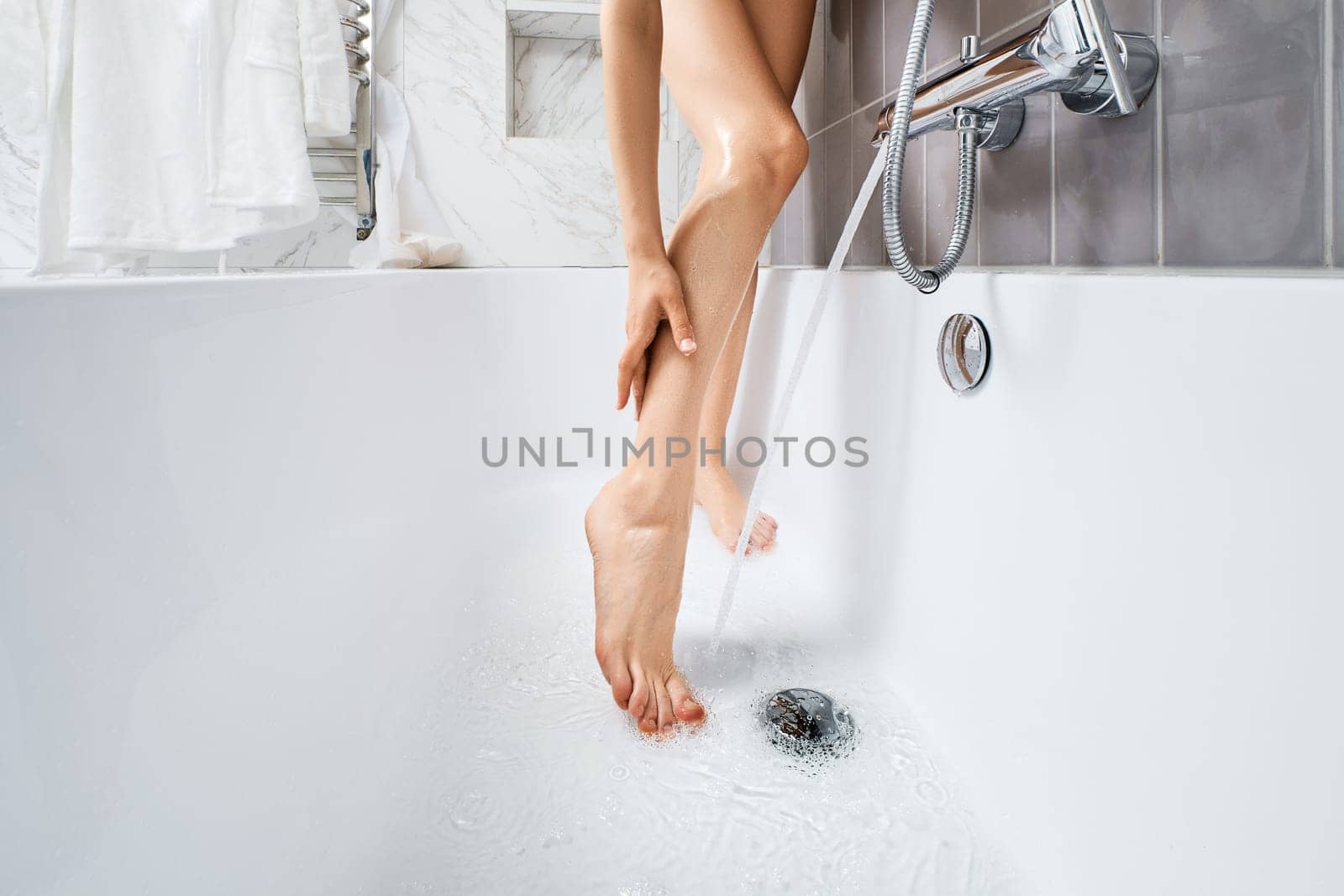 Unrecognizable young woman washing her legs in bathtub