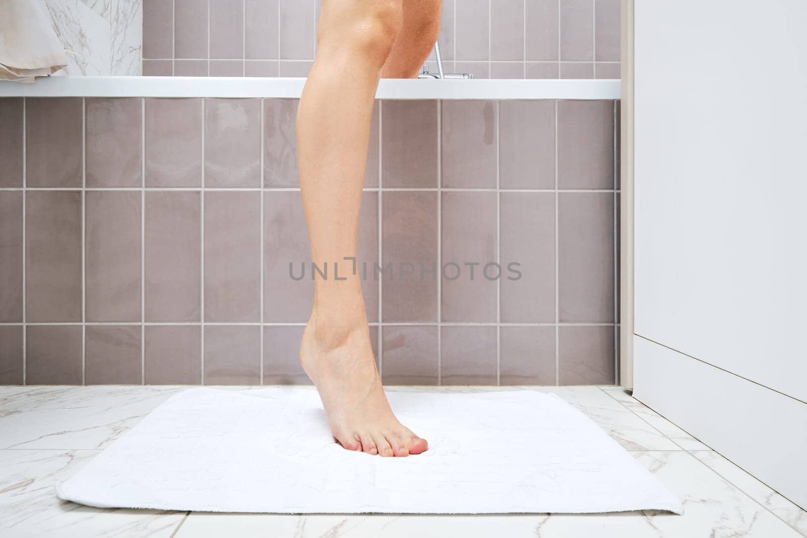 Unrecognizable young woman is stepping over edge of bathtub on a towel thrown on the floor after taking bath