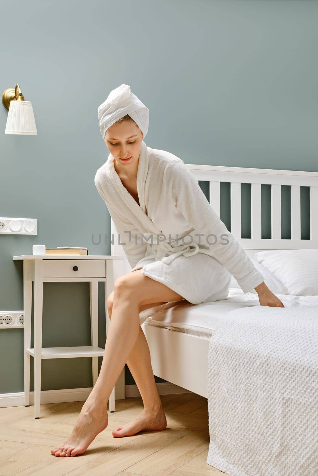 Young woman in bathrobe sits on the bed in the bedroom