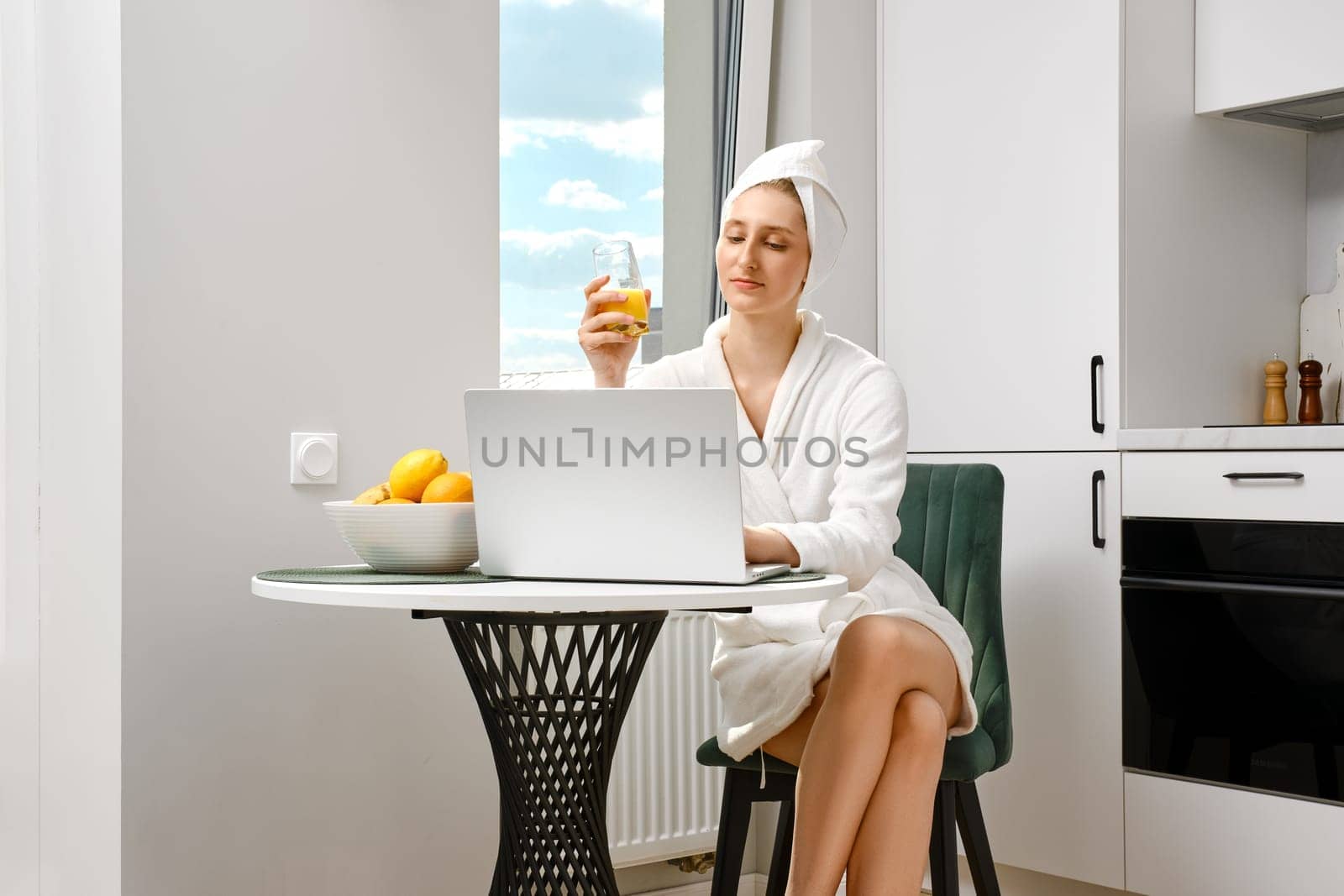 Young woman wearing bathrobe checking mail while having breakfast
